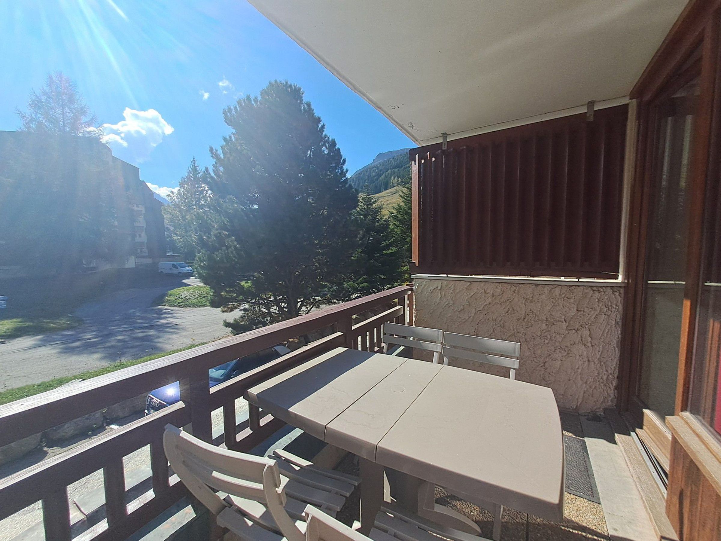A balcony with a table and chairs, overlooking a parking area and trees.
