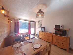 Een gezellige eethoek met een houten tafel gedekt voor twee personen, een televisie op een houten kast en een plafondlamp.