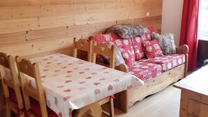 Una habitación acogedora con pared de madera, un sofá con funda estampada de corazones, una mesa con una funda similar y dos lámparas fijadas a la pared.