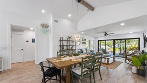 A spacious dining area with a wooden table and chairs, a chandelier, and a view of the outdoors through large windows.