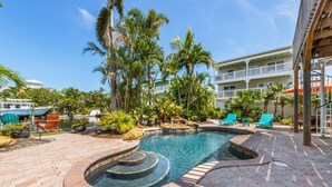 A pool area with a hot tub, lounge chairs, and palm trees.