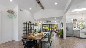 A spacious kitchen with modern appliances, a dining area with a wooden table and chairs, and a view of the outdoors through large windows.