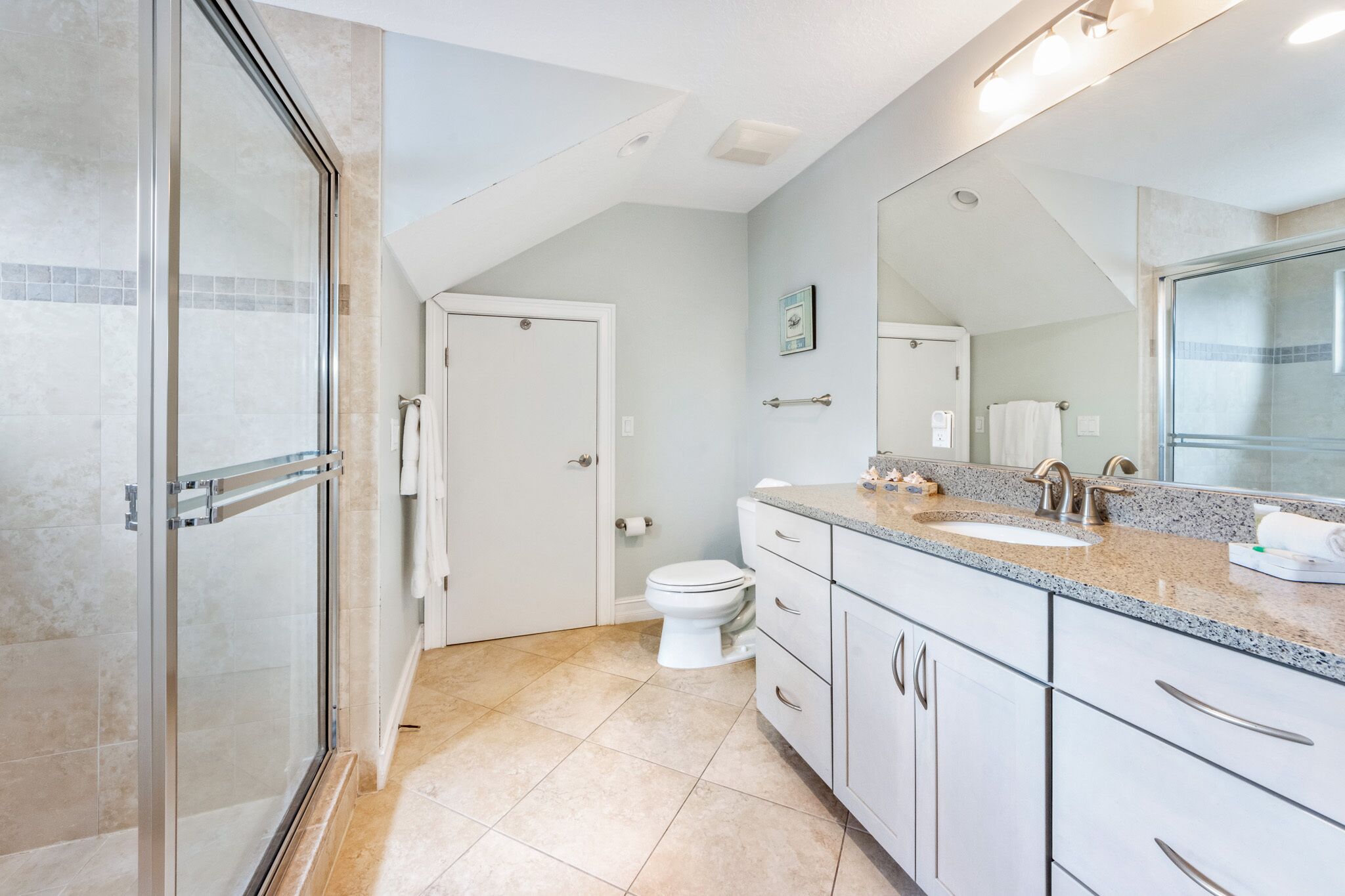 Un baño moderno con cabina de ducha de vidrio, inodoro blanco y lavamanos con encimera de granito.