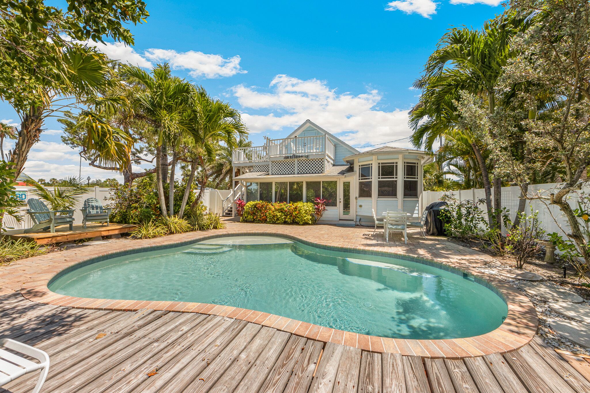 A backyard with a swimming pool, wooden deck, and a house with a balcony.