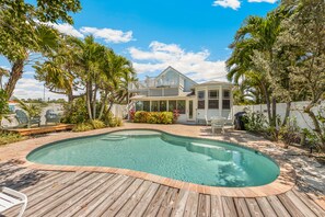 Un jardin avec une piscine, une terrasse en bois et une maison dotée d’un balcon.