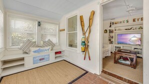 Une pièce avec un coin lecture près d’une fenêtre, un téléviseur et une étagère contenant des livres et des objets décoratifs.