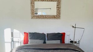 Ein Schlafzimmer mit einem Bett, Kissen, einem Nachttisch, einer Lampe und einem Spiegel an der Wand.