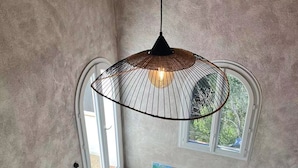 Ein gemütlicher Raum mit schrägem Dach, einer schwarzen Pendelleuchte, einem Fenster mit Ausblick, einer Couch mit gemusterten Kissen und einem Teppich mit geometrischen Mustern.