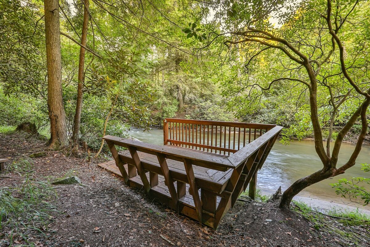 Un banc en bois, situé dans une zone boisée, avec une rivière en arrière-plan.