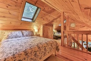 A wooden cabin bedroom with a bed, a skylight, and a view of the outdoors. - Romance on The Cartecay | Ellijay, GA (Ellijay)
