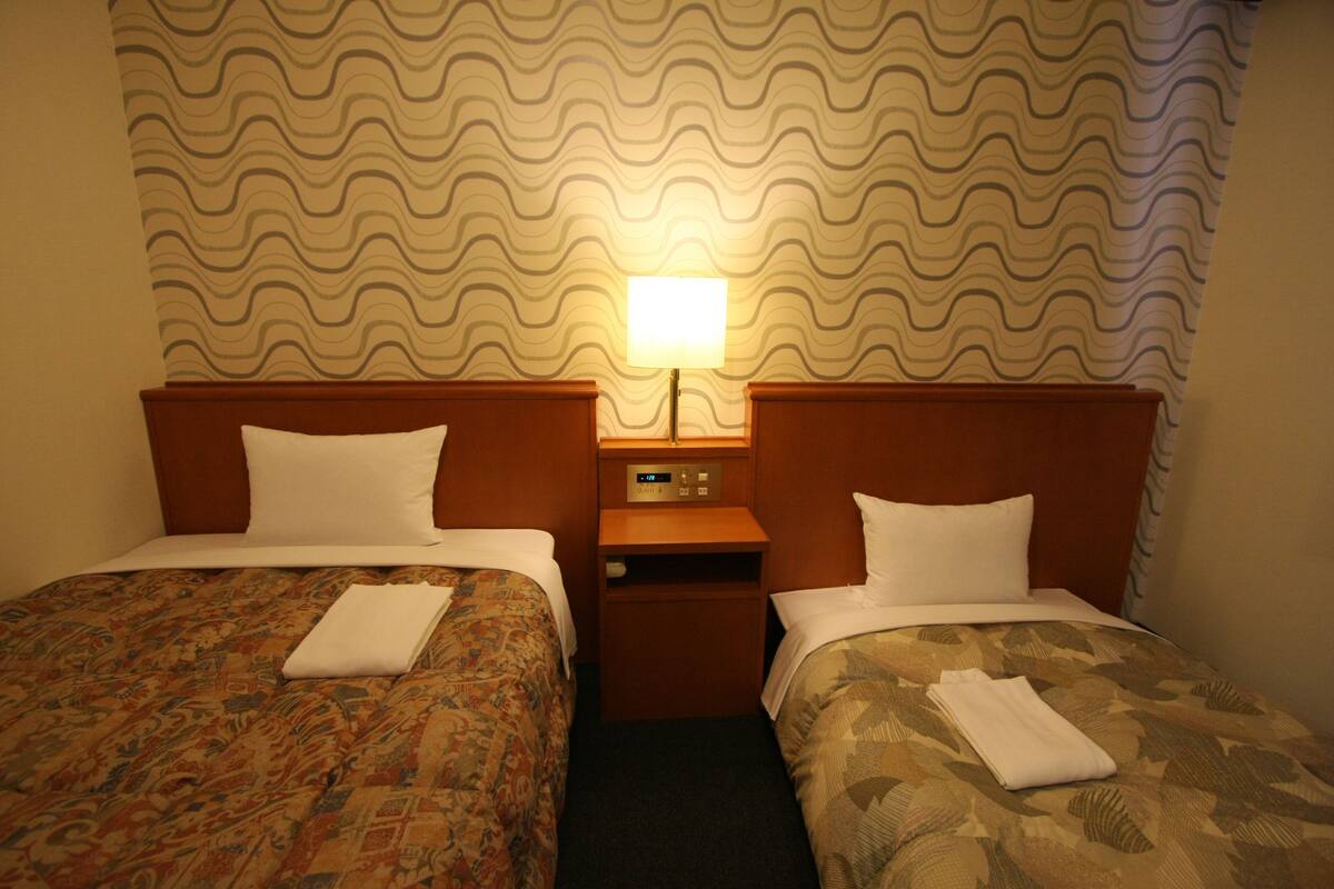Une chambre d’hôtel avec deux lits, une table de chevet et une horloge murale.