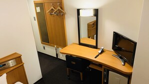Habitación de hotel con un escritorio de madera, un espejo, un televisor, un mueble pequeño y una cama con edredón estampado de flores.