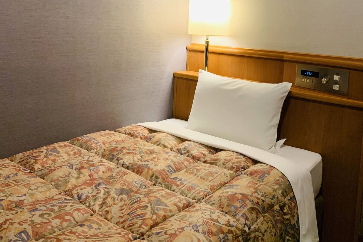 Une chambre d’hôtel avec un lit bien fait, une lampe de chevet et une horloge numérique sur la table de chevet.