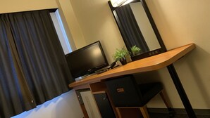 Habitación de hotel con escritorio, televisión, lámpara y planta en maceta.