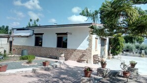 A two-story building with a stone base and white upper walls, featuring a small porch with potted plants and outdoor seating. - Mapagog: CASA PIXAVI, Surrounded by orange trees between the mountains and the beach <br> (Castello)