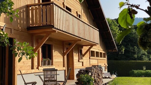 A wooden chalet with a balcony, a table, and chairs outside.