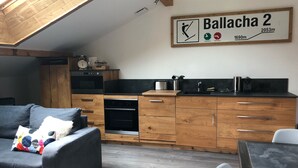 A modern kitchen with wooden cabinets and a black countertop, a dining area with a table and chairs, and a loft bedroom with a sloped ceiling.