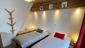 A room with two beds, a wooden ceiling, and a wall-mounted light fixture.