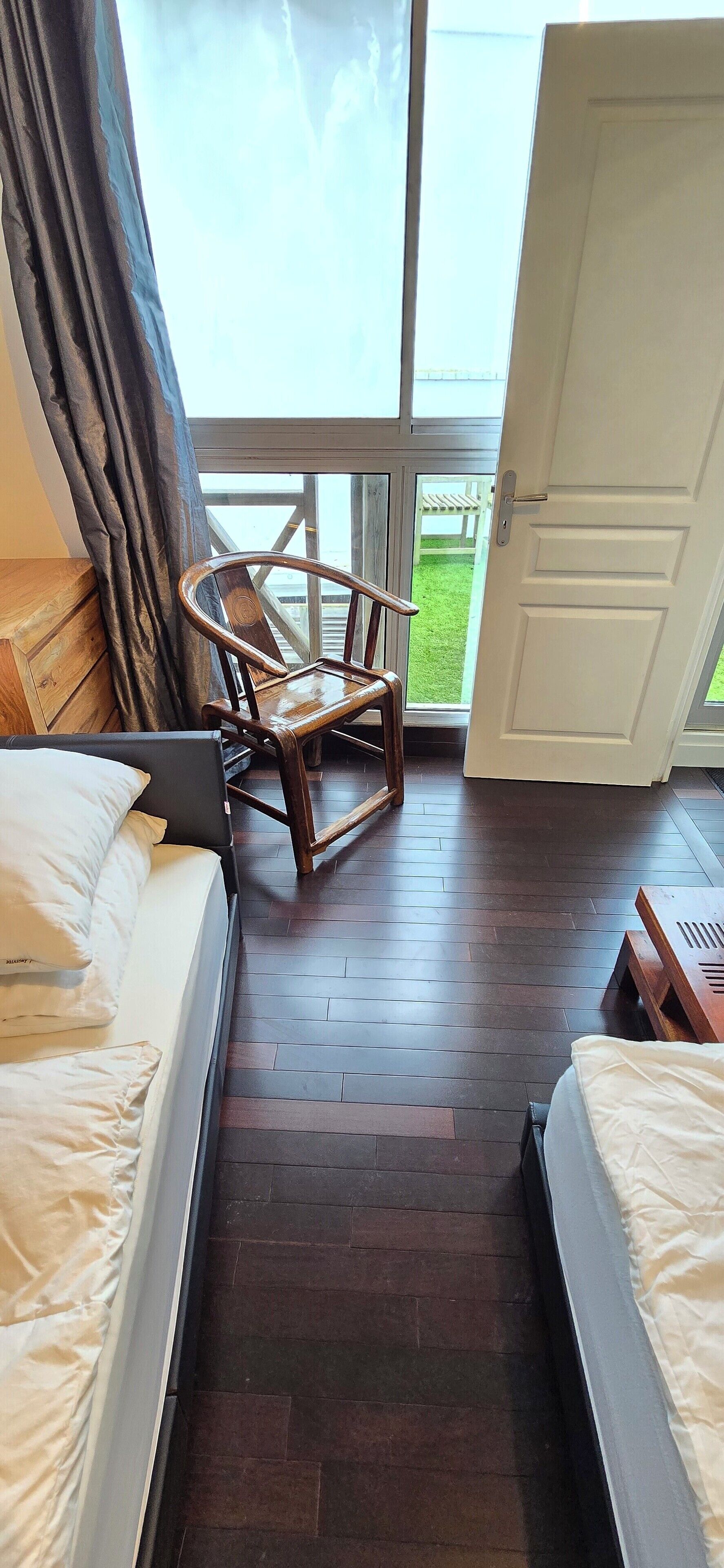 A hotel room with two beds, a wooden chair, and a large window offering a view of a grassy area.