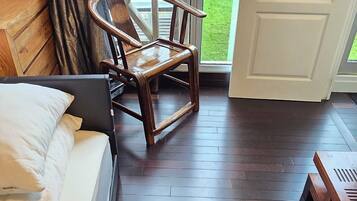 A hotel room with two beds, a wooden chair, and a large window offering a view of a grassy area.