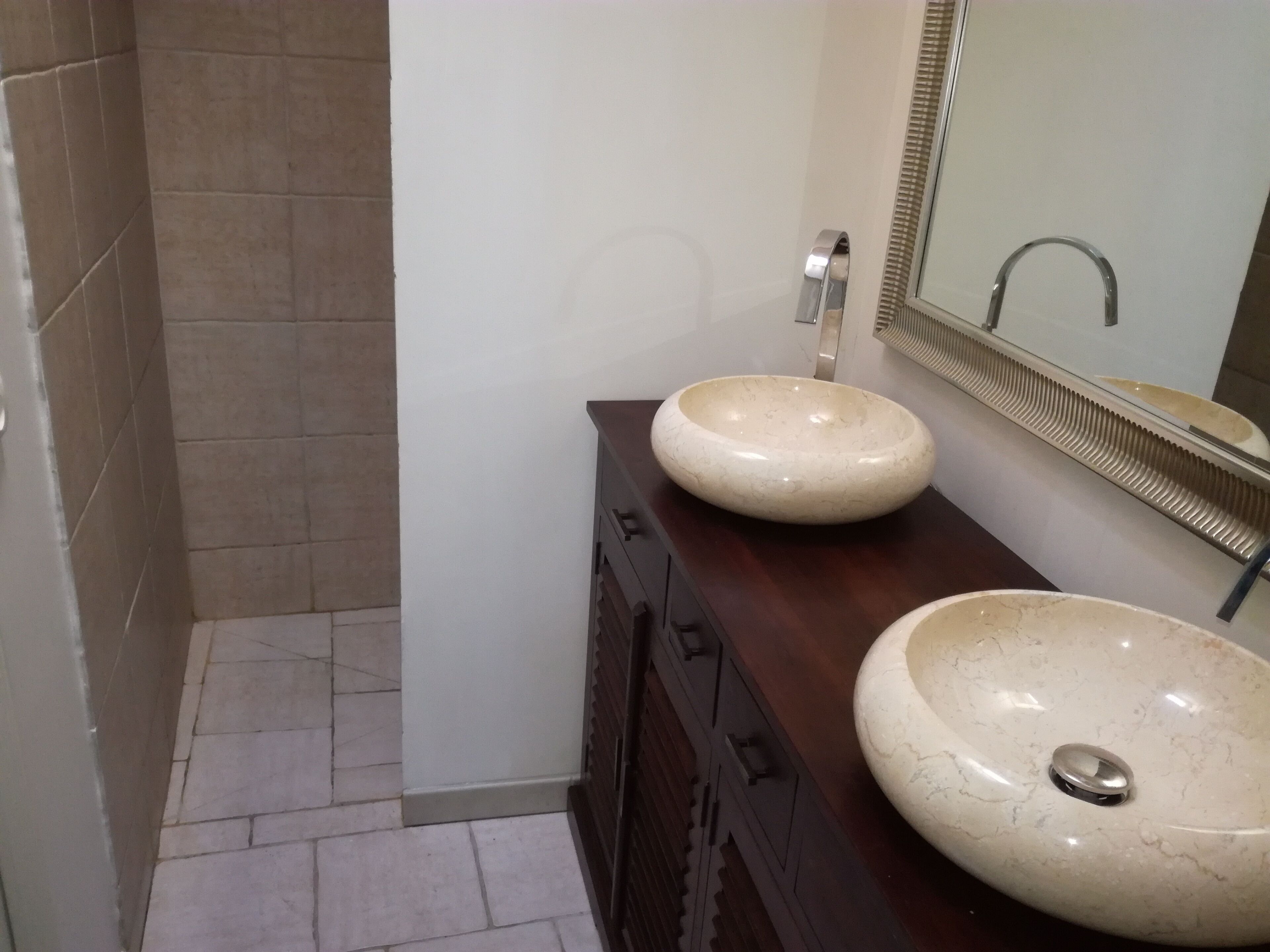 A bathroom with two round marble sinks, a dark wooden vanity, and a mirror with a metallic frame.