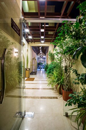 Un couloir d’hôtel avec un ascenseur en verre, des plantes en pot et un panneau indiquant une zone réservée au personnel.