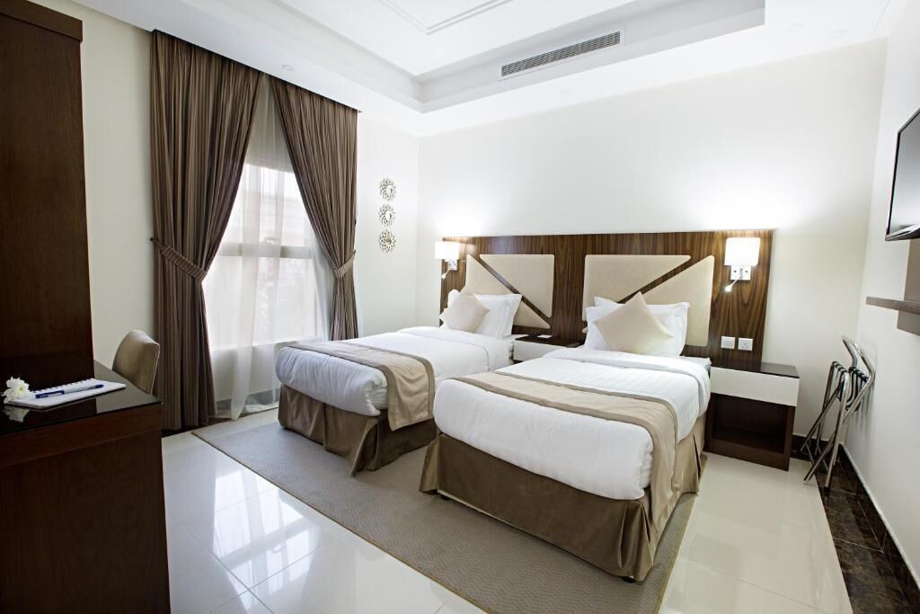 A hotel room with two beds, a desk, and a TV.