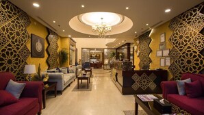 Un vestíbulo de hotel con mostrador de recepción central, sofás y una araña.