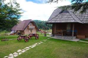 Situated in a lush landscape, this cabin features a porch with benches and a traditional cart, inviting relaxation and socializing.