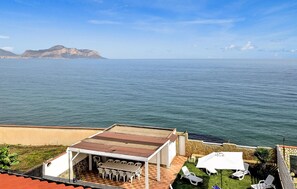 Relax on the coastal terrace with a view of the sea and distant mountains, featuring outdoor seating and a covered area.