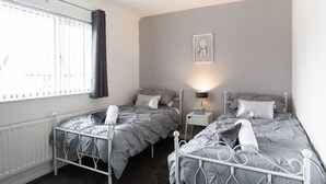 Ein Schlafzimmer mit zwei Betten, einem Nachttisch mit Lampe, einem Heizkörper und einem Fenster mit Vorhängen.