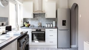 Eine moderne Küche mit weißen Schränken, einem Edelstahlkühlschrank, einem eingebauten Backofen und einer Waschmaschine.