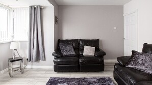 Ein modernes Wohnzimmer mit einem schwarzen Ledersofa, einem kleinen Beistelltisch mit einer Lampe und einem grauen Vorhang.