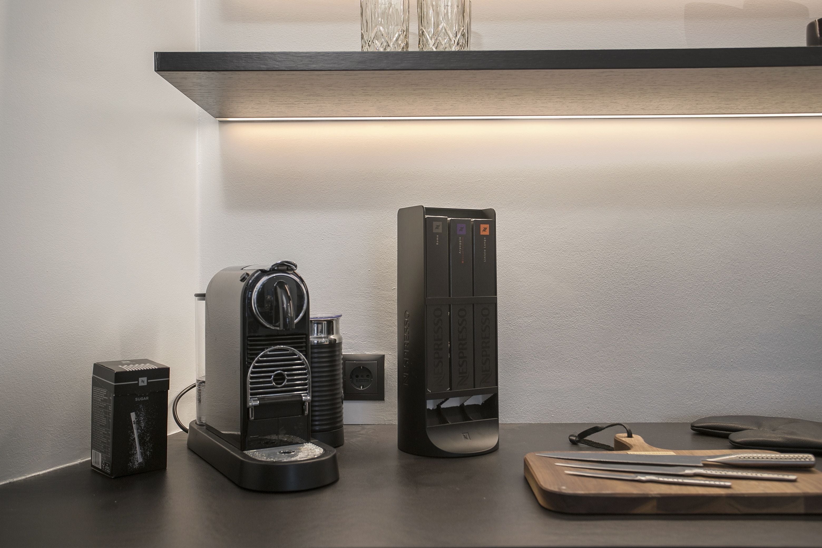 Eine Küchenzeile mit einer Kaffeemaschine, einer Nespresso-Maschine und einem Schneidebrett mit Besteck.