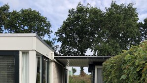A modern house with a covered patio, large windows, and a gravel driveway. - Cottage coast in South Holland behind the dunes by the sea (Ouddorp)