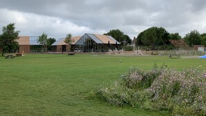 A spacious outdoor area with a grassy field, a wooden structure, and a modern building with large windows. - Cottage coast in South Holland behind the dunes by the sea (Ouddorp)
