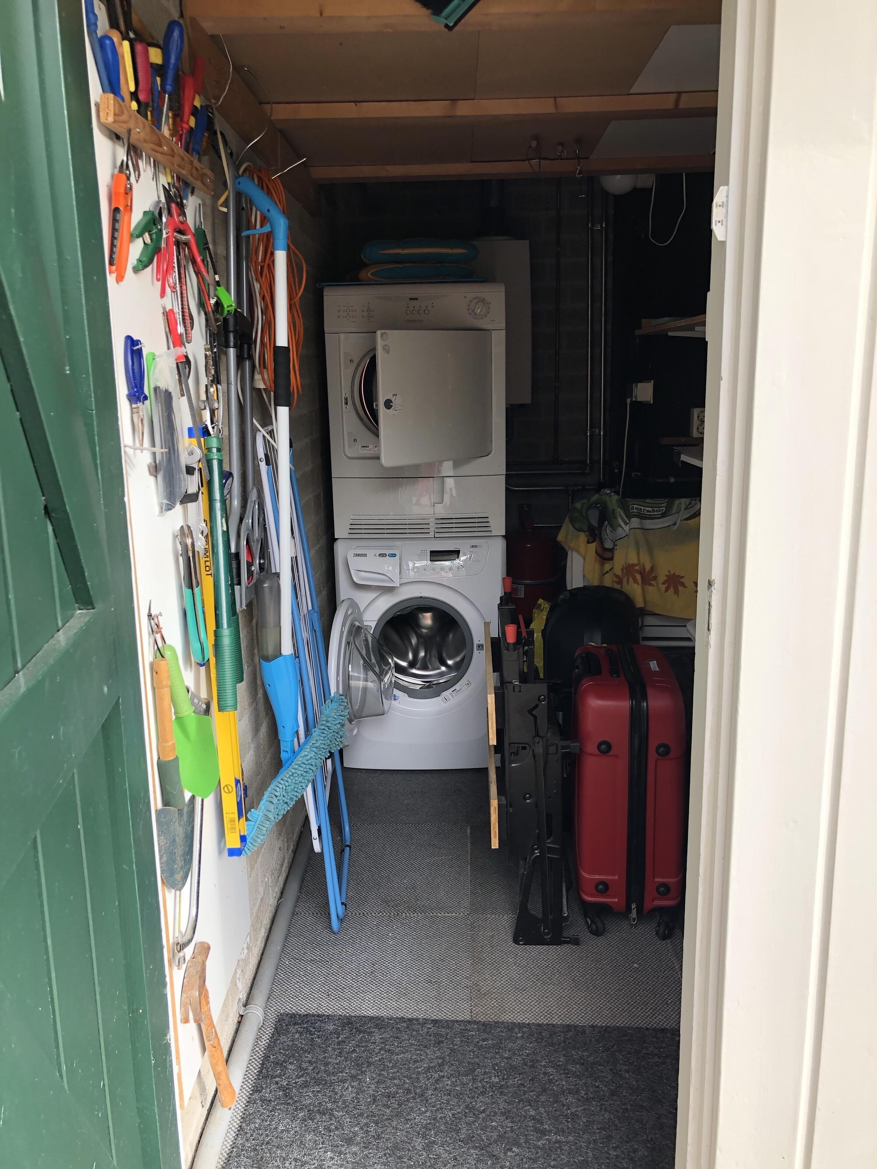 Une buanderie équipée d’un lave-linge, d’un sèche-linge et de divers outils accrochés au mur.