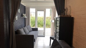 A living room with a sofa, a cabinet, and a view through a glass door. - Cottage coast in South Holland behind the dunes by the sea (Ouddorp)