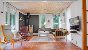 A spacious living room with a fireplace, large windows, a television, and a tiled floor.