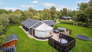 A modern house with a large glass conservatory, a wooden deck, and a trampoline in a lush green backyard.