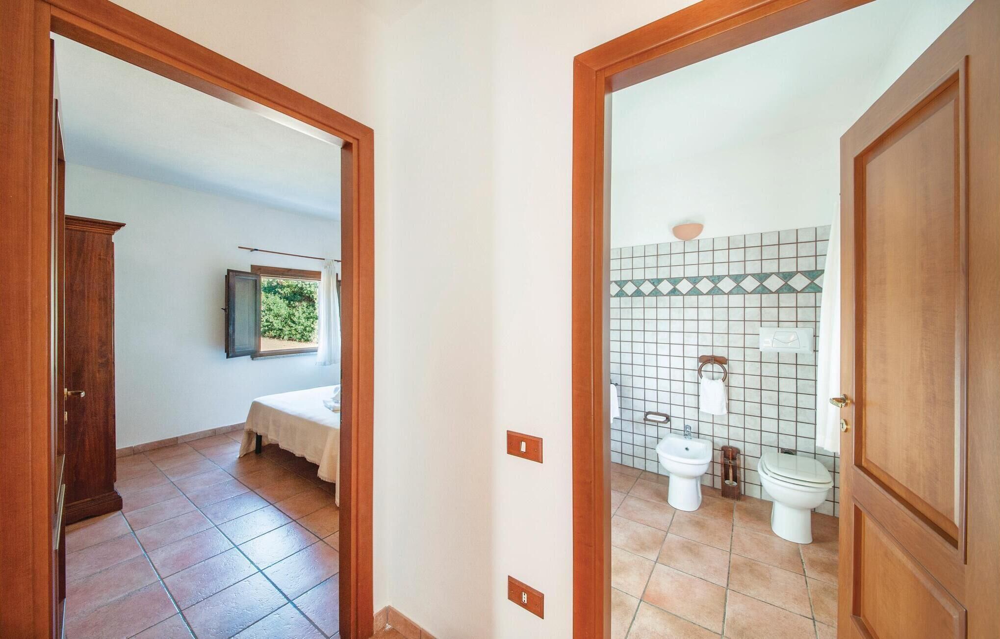 A hallway leading to a bedroom with a bed and a window, and a bathroom with a toilet, bidet, and tiled walls.