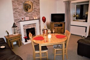 A living room with a fireplace, a dining table with chairs, a television, and a window with curtains.