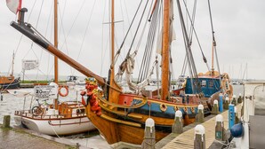 Um barco de madeira atracado num cais, com um círculo boia e um aviso a indicar serviço de navegação diário.