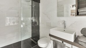 Een moderne badkamer met een douche met glazen wand, een witte wastafel en een toilet.