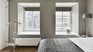 Een slaapkamer met een bed, een radiator, een raam met uitzicht, een nachtkastje met een lamp en een kapstok.