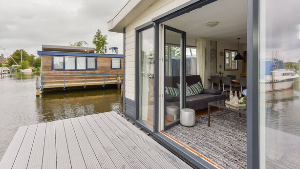 A modern houseboat with a deck, a living area with a sofa and coffee table, and a glass door leading to a bedroom. - Bright and Comfortable Houseboat (Aalsmeer)