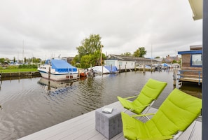 A dock with green lounge chairs and a small grey ottoman. Boats are docked in the background. - Bright and Comfortable Houseboat (Aalsmeer)