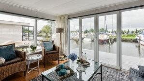 A modern living room with large windows overlooking a marina. - Bright and Comfortable Houseboat (Aalsmeer)