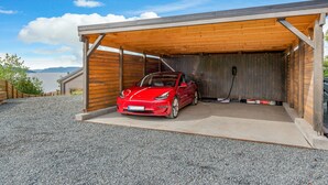 A red sports car parked inside a covered garage with a view of the mountains. - The Oceanfront (Trondheim)