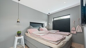 A modern bedroom with a grey bed, white nightstand, and a hanging plant. - The Oceanfront (Trondheim)